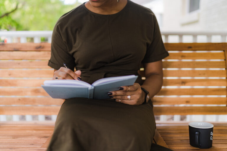 A woman writes in a notebook on a bench.