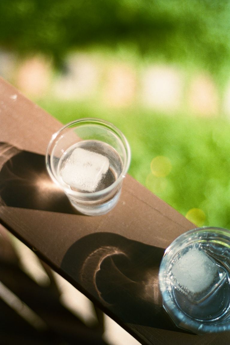 Two glasses of ice water sit on a wooden ledge.