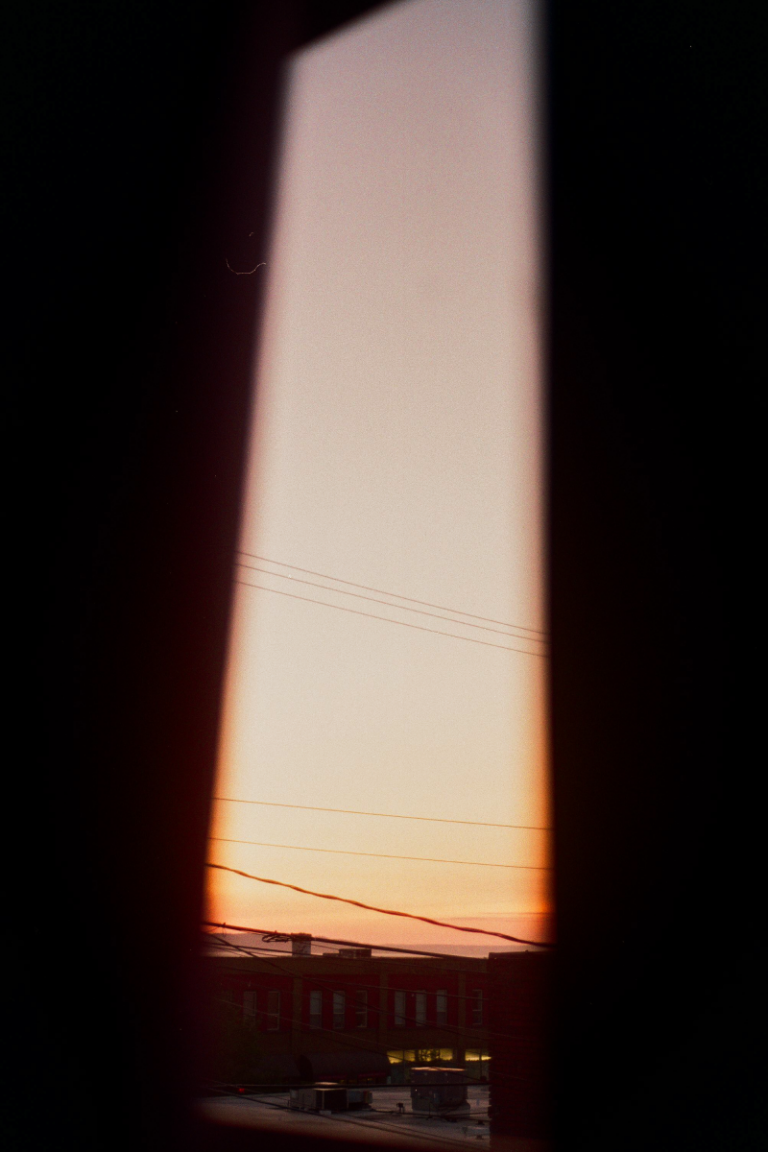 Telephone lines, the top of buildings, and an orange evening sky visible through a window.