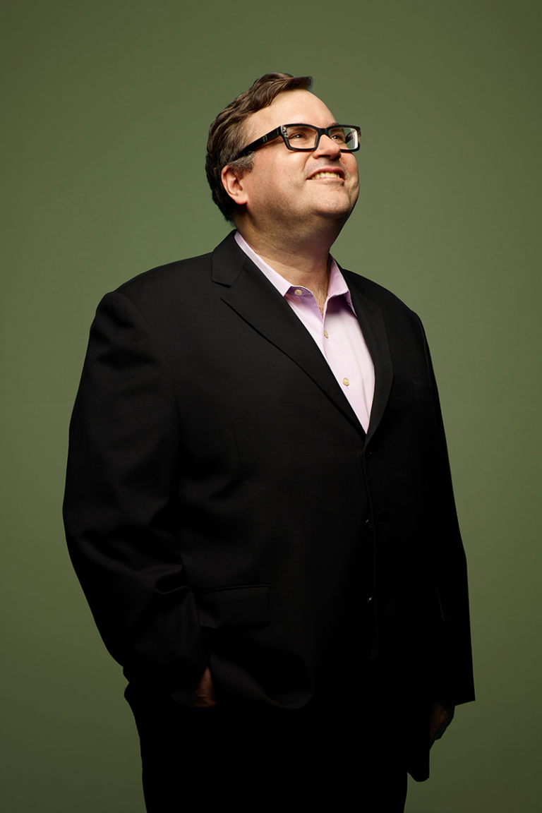 Reid Hoffman stand smiling while looking up to something above him and out of frame.