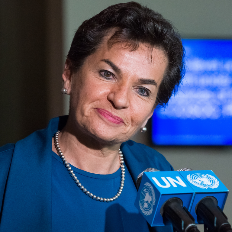 Christiana Figueres in front of a microphone with the United Nations symbol.