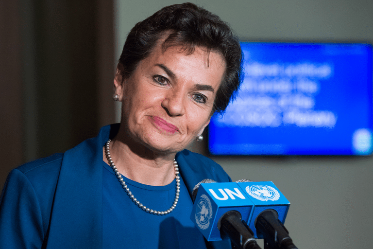 Christiana Figueres in front of a microphone with the United Nations symbol.