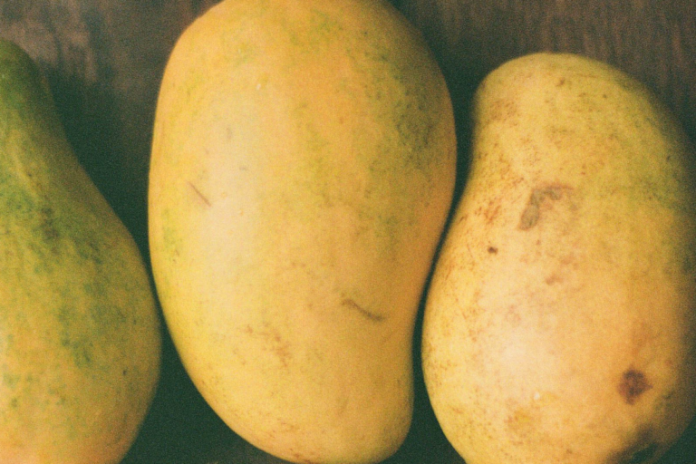 Four mangoes on a wooden surface.
